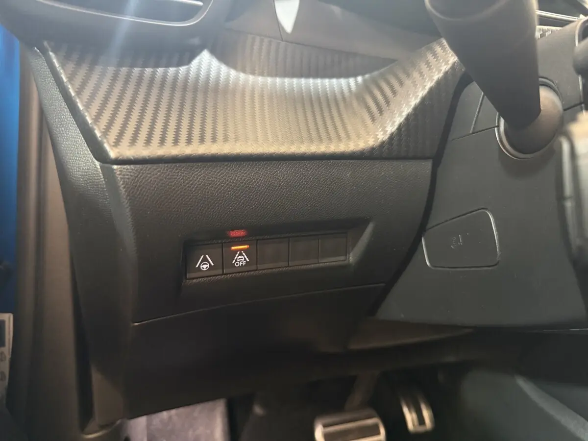 Détail du tableau de bord côté gauche avec boutons d’aide à la conduite et finition effet carbone sur Peugeot 2008 bleu.