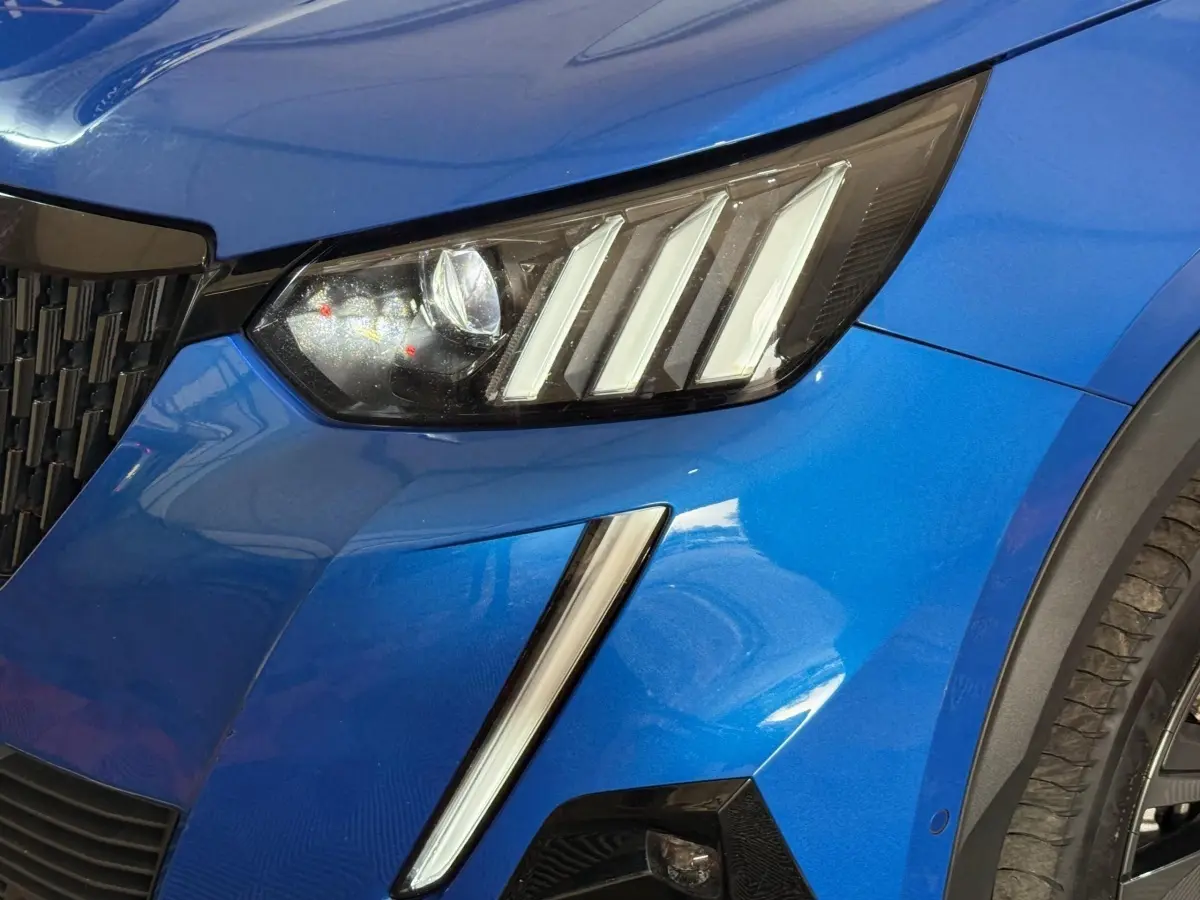 Gros plan sur le phare avant droit et la calandre d’un Peugeot 2008 bleu métallisé, détails LED visibles.