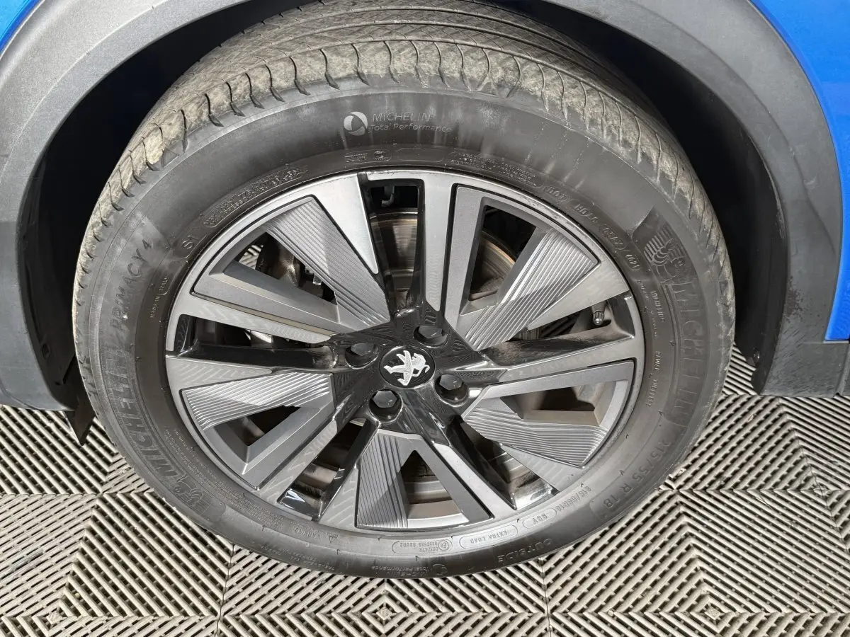 Gros plan sur la roue avant droite d’un Peugeot 2008 bleu, mettant en valeur la jante alliage au design moderne.