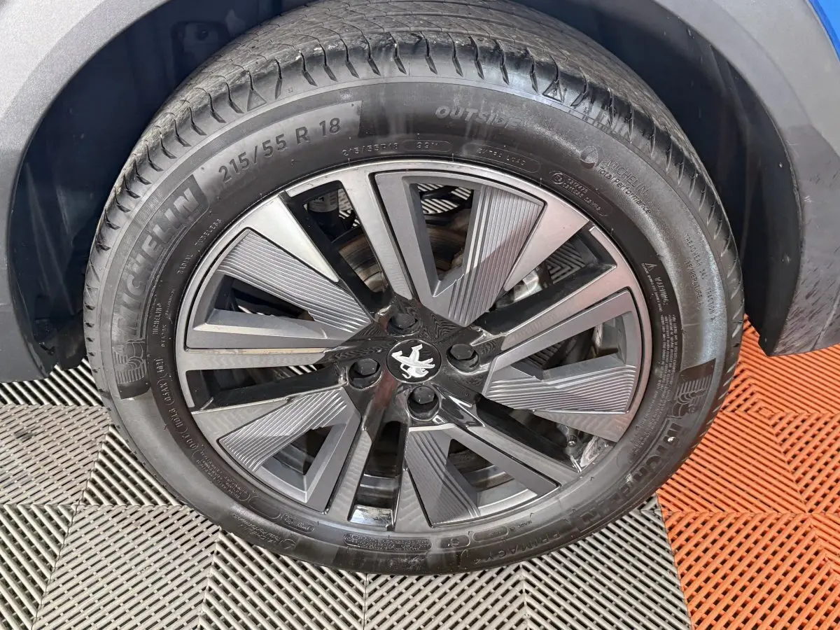 Gros plan sur la roue avant droite d’un Peugeot 2008 bleu, jante alliage noire et grise au design moderne.
