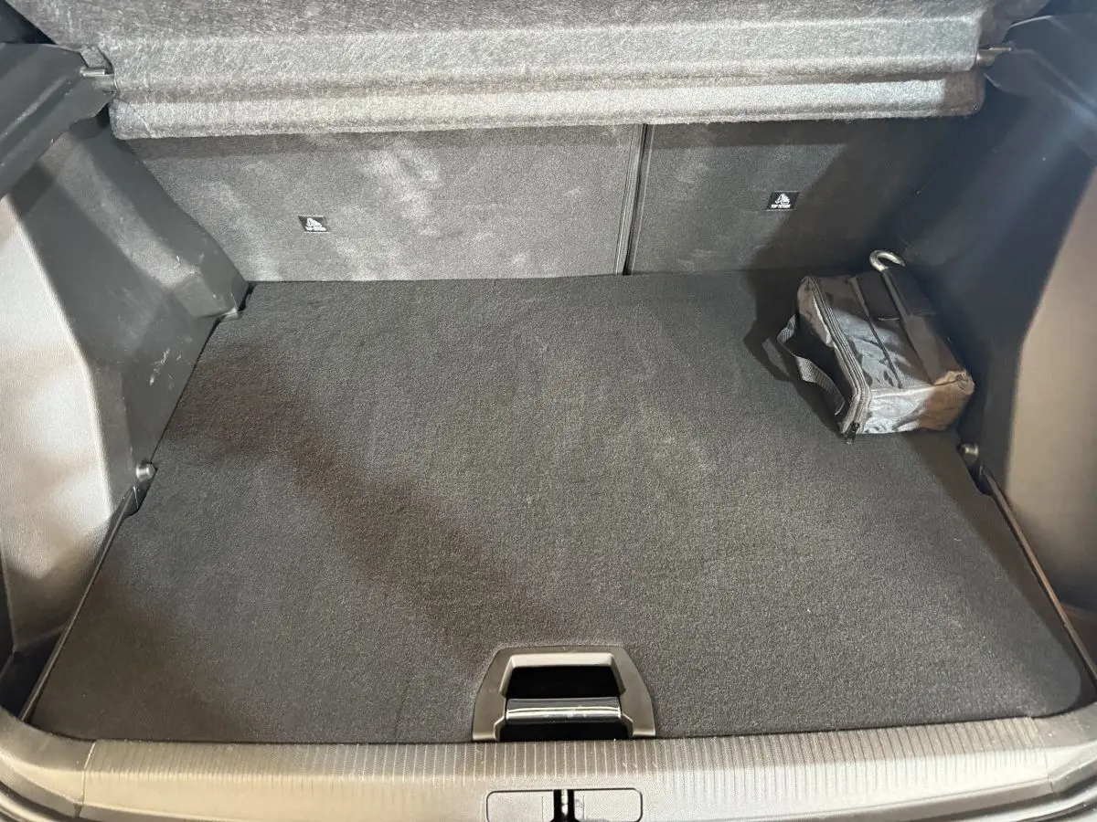Coffre ouvert du Peugeot 2008 bleu, vue de dessus montrant un espace de rangement propre avec sac noir à droite.