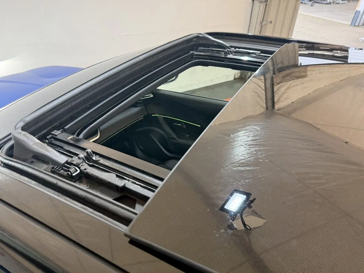 Toit ouvrant panoramique ouvert sur Peugeot 2008 bleu, vue rapprochée du mécanisme et intérieur avec éclairage d'ambiance visible.