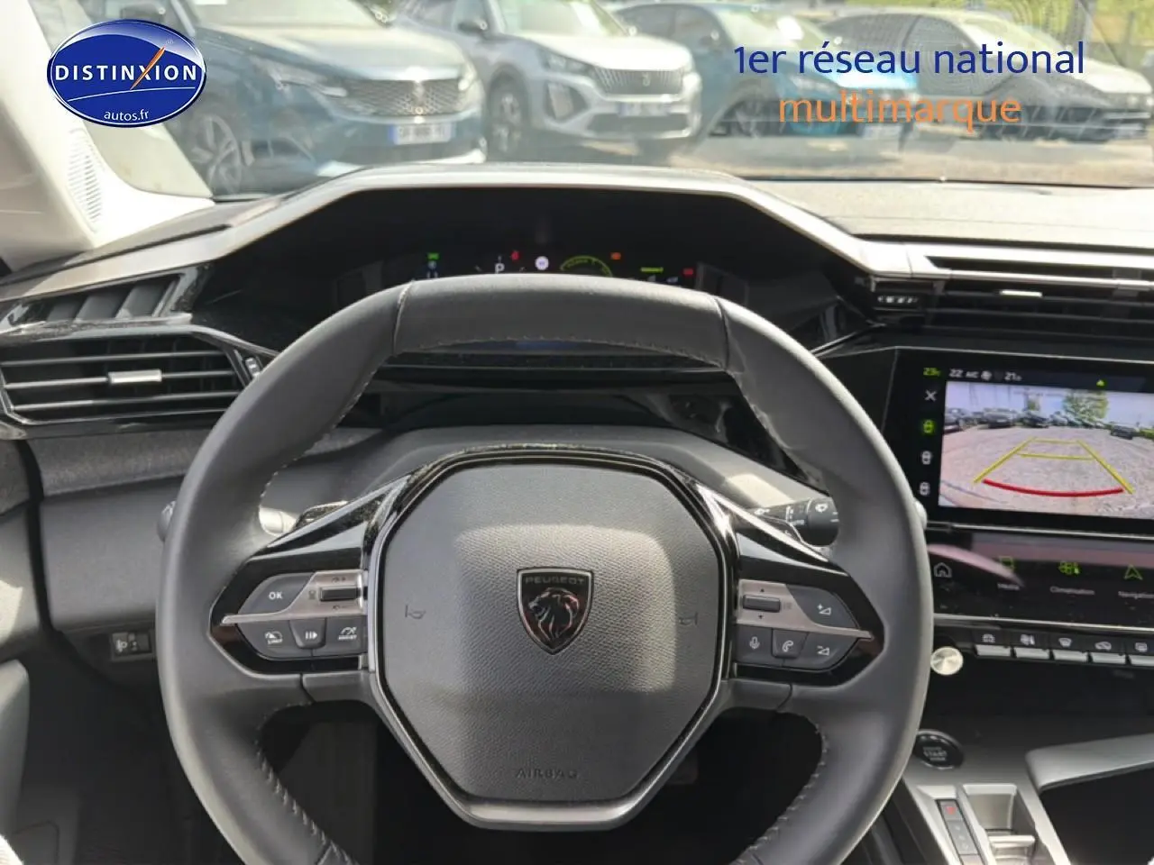 Vue intérieure centrée sur le volant cuir noir de la Peugeot 408 Hybrid 136 avec écran tactile affichant la caméra de recul.