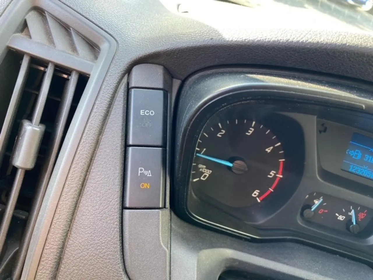 Gros plan sur le tableau de bord du Ford Transit Fourgon orange, montrant le compte-tours et les boutons de contrôle ECO et radar de stationnement.