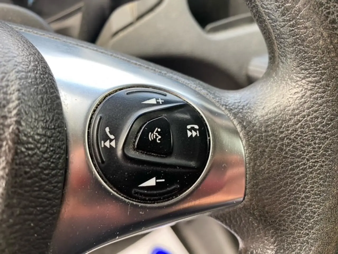 Gros plan sur les commandes audio et téléphone intégrées au volant noir du Ford Transit Fourgon orange de 2015.