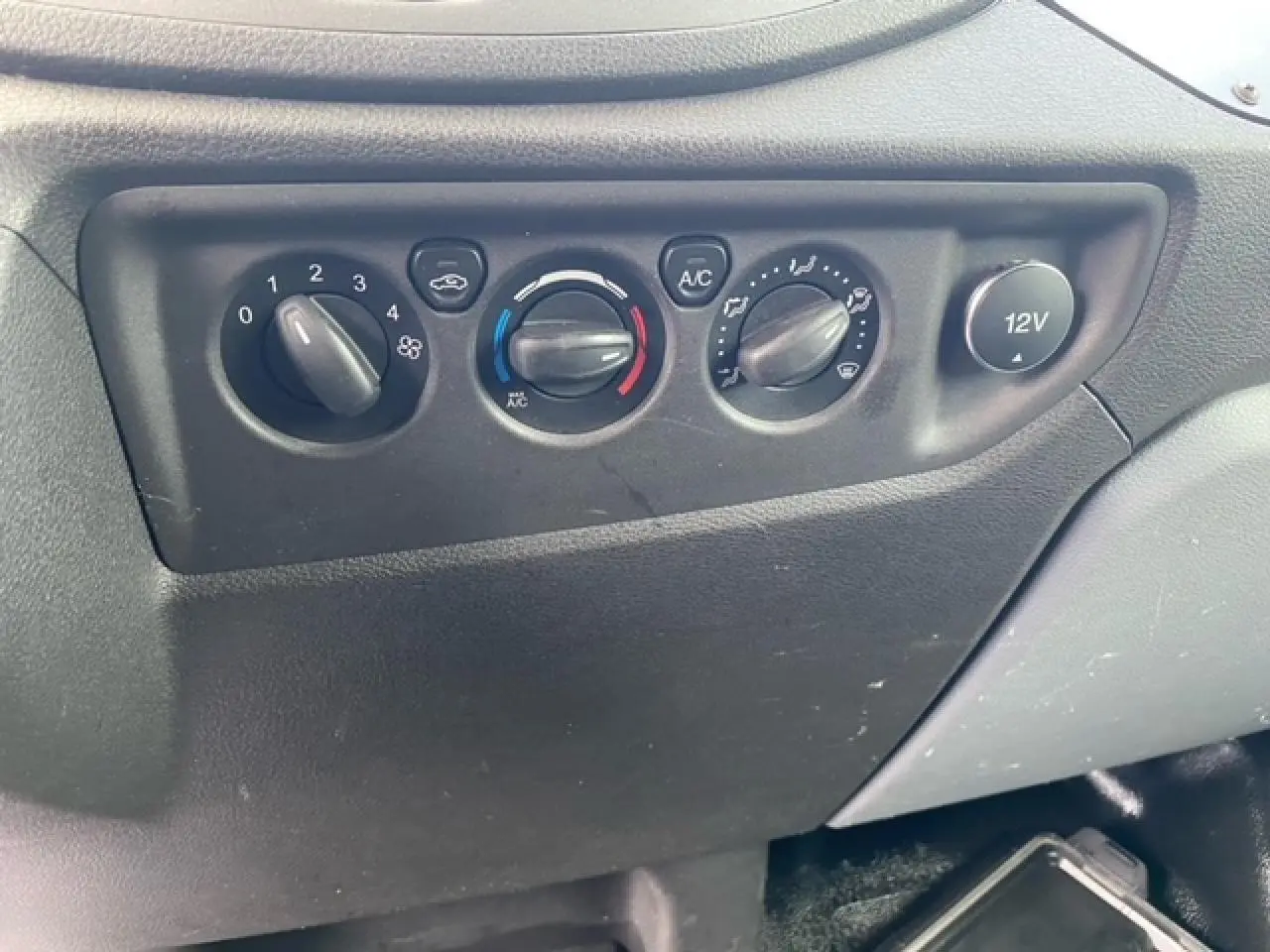 Gros plan sur les commandes de climatisation et prise 12V du tableau de bord du Ford Transit Fourgon L3H2 2015.