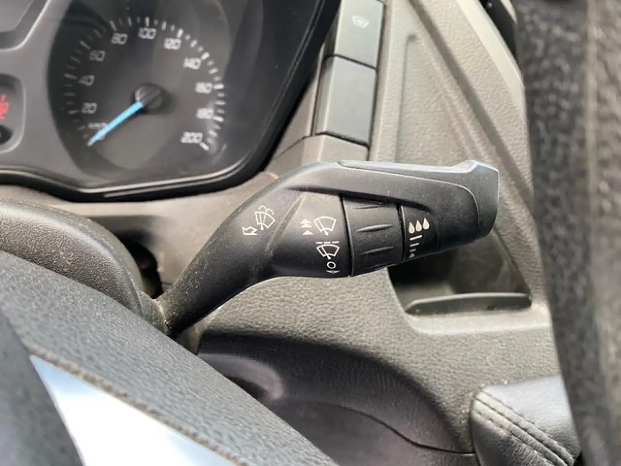 Gros plan sur la commande des essuie-glaces à droite du volant dans le tableau de bord noir du Ford Transit Fourgon orange.