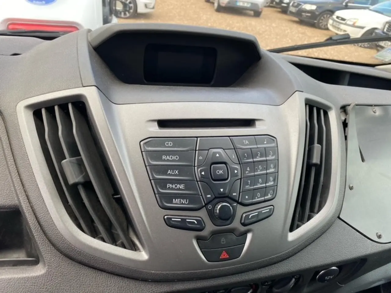 Vue rapprochée du tableau de bord gris du Ford Transit Fourgon 2015 avec commandes audio et aérateurs centraux.