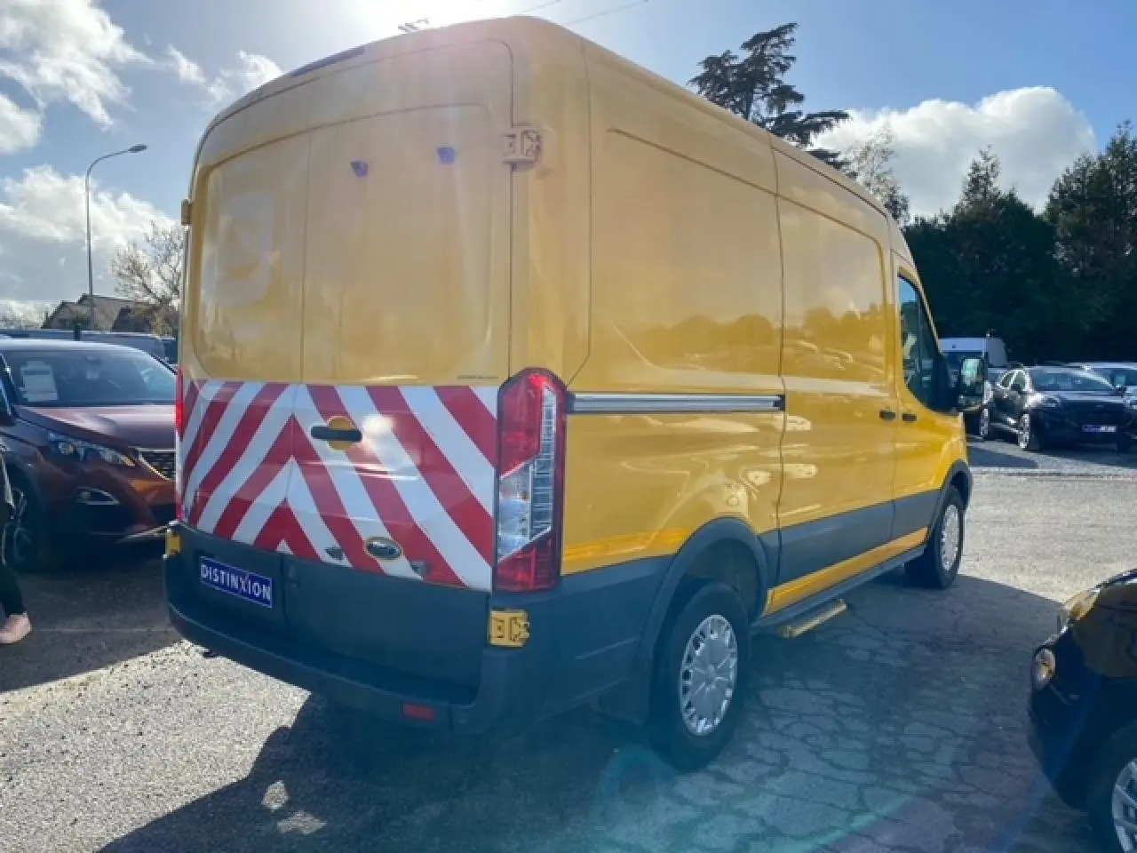 Vue 3/4 arrière droite d’un Ford Transit fourgon orange avec bandes réfléchissantes rouges et blanches sur les portes arrière.