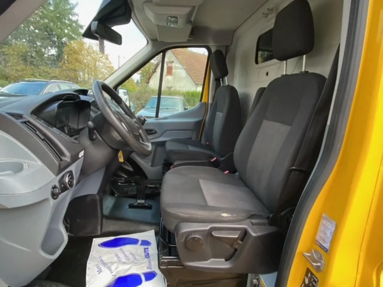 Vue intérieure côté conducteur du Ford Transit Fourgon orange, montrant les sièges avant et le tableau de bord.
