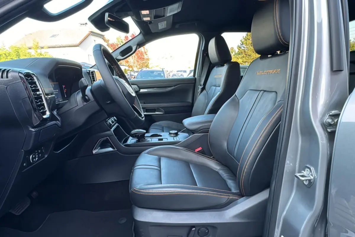 Vue intérieure côté conducteur du Ford Ranger PHEV 281 Wildtrak gris iconic avec sièges cuir noirs et surpiqûres orange.