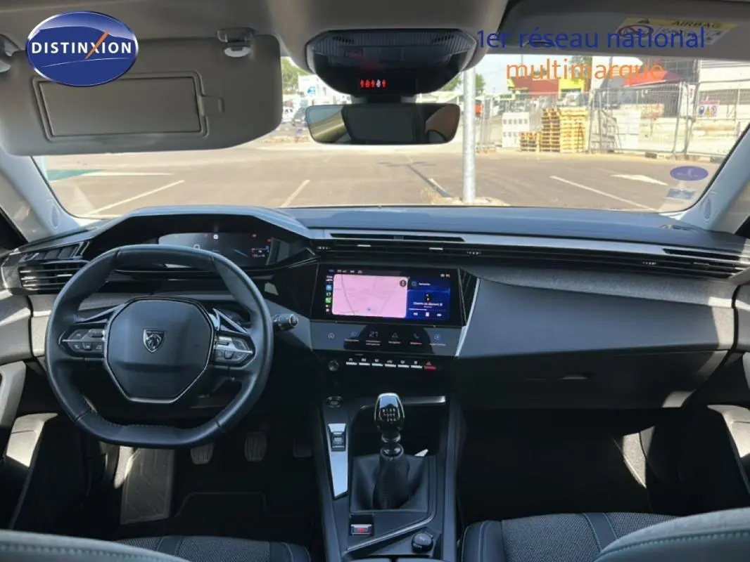 Vue intérieure frontale du poste de conduite de la Peugeot 308 bleu clair, avec volant compact, écran tactile et levier de vitesses manuel.