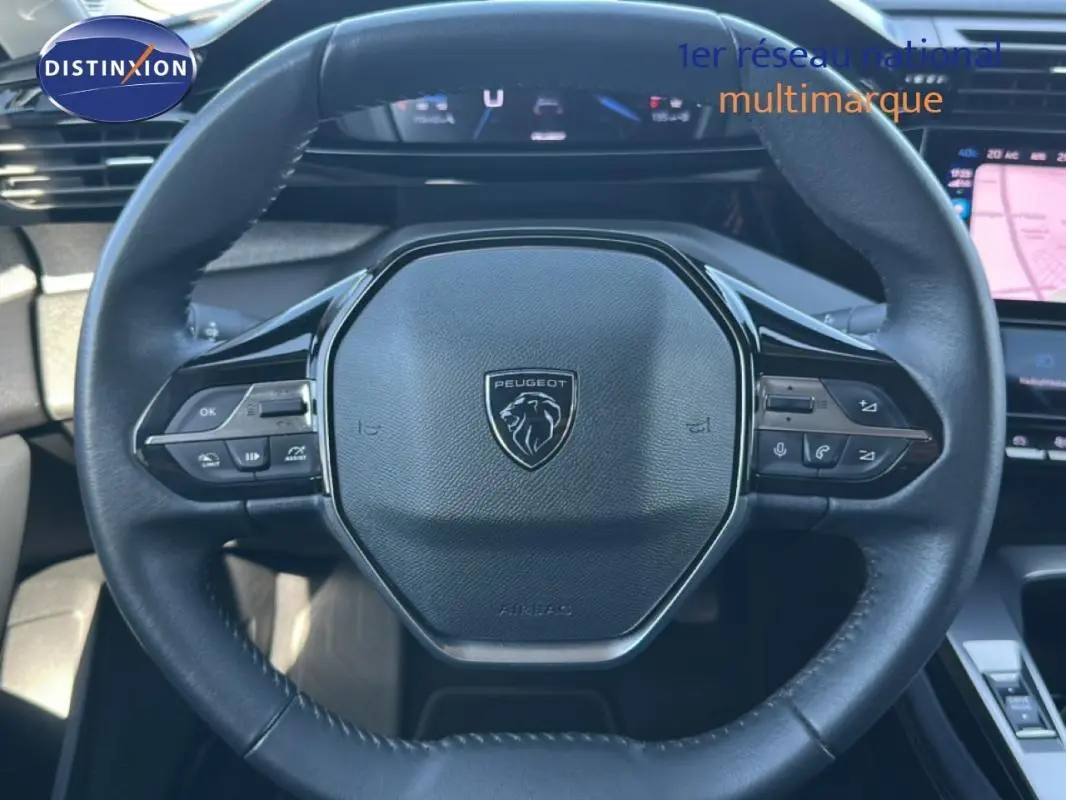 Vue rapprochée du volant cuir noir de la Peugeot 308 2021 avec commandes intégrées et tableau de bord numérique en arrière-plan.