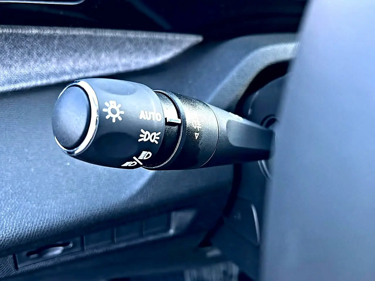 Gros plan sur la commande des phares noire à gauche du volant dans l’habitacle d’une Peugeot 308 SW noire.
