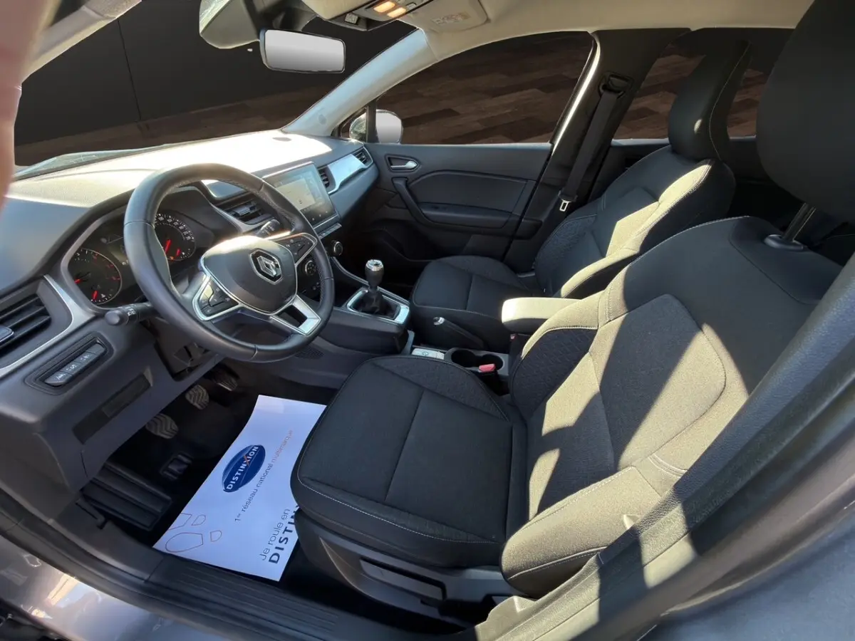Vue intérieure côté conducteur du Renault Captur gris foncé 2024, montrant le volant cuir, tableau de bord et sièges tissu noirs.