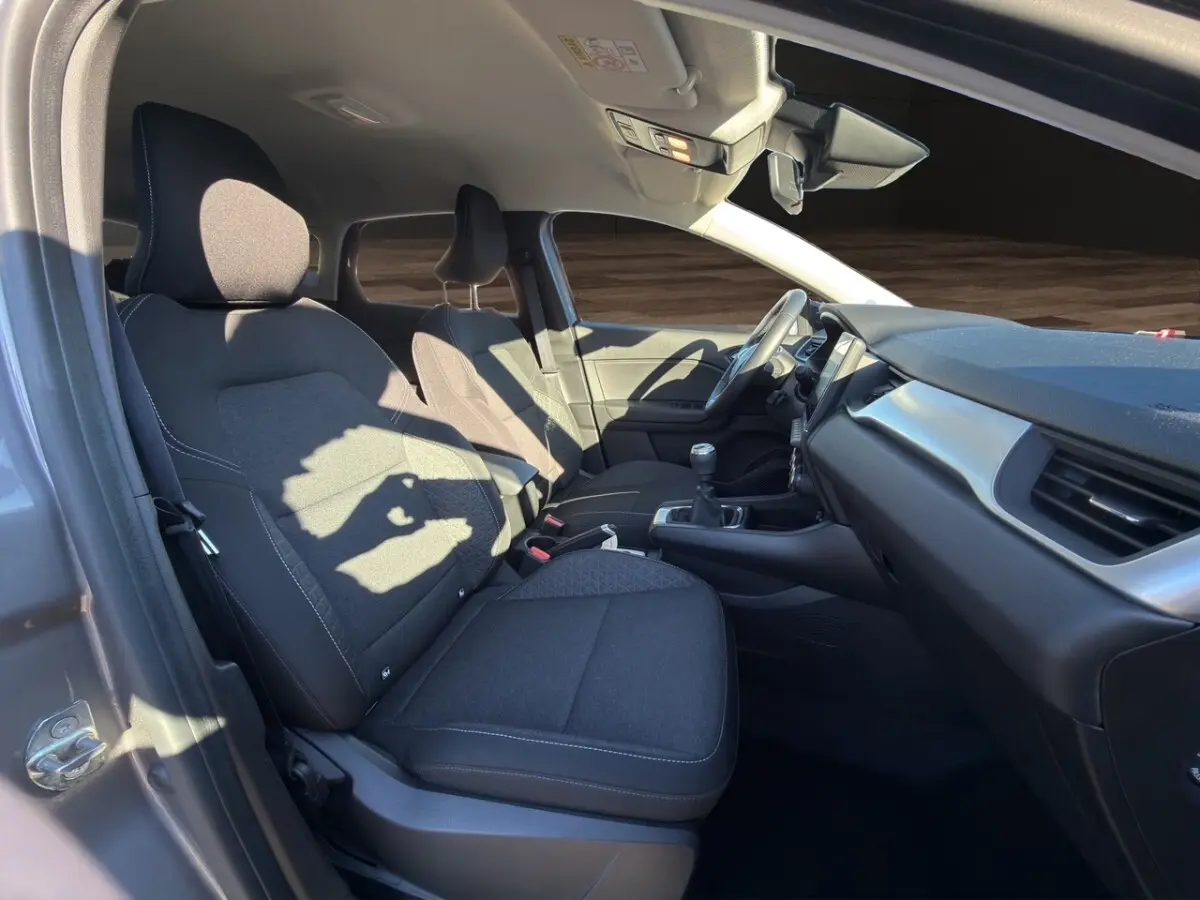 Intérieur avant droit du Renault Captur gris foncé 2024, sièges tissu noirs et tableau de bord moderne avec boîte manuelle.