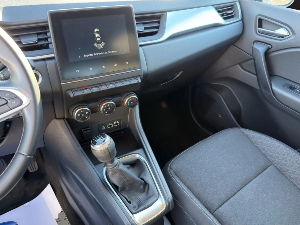 Vue intérieure côté passager du Renault Captur gris foncé 2024, avec écran tactile central et levier de vitesse manuel.