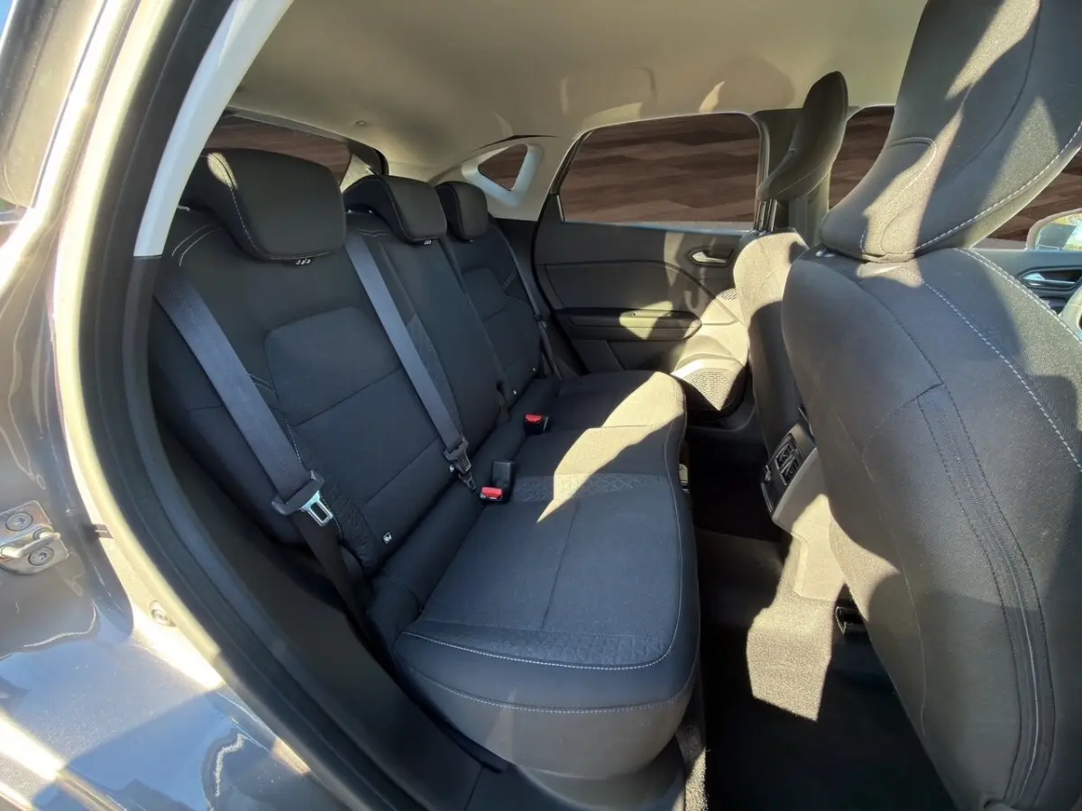 Vue intérieure côté arrière droit du Renault Captur gris foncé 2024, montrant la banquette arrière et les sièges avant en tissu noir.