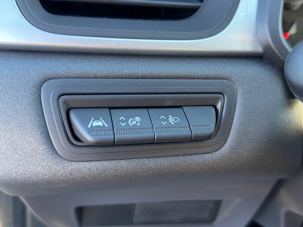Gros plan sur les boutons de réglage des aides à la conduite et des phares du tableau de bord d’un Renault Captur gris foncé 2024.