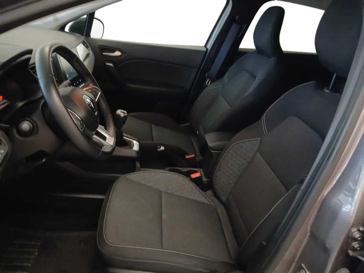 Intérieur avant droit du Renault Captur gris foncé 2024, sièges tissu noirs et volant multifonctions cuir synthétique.