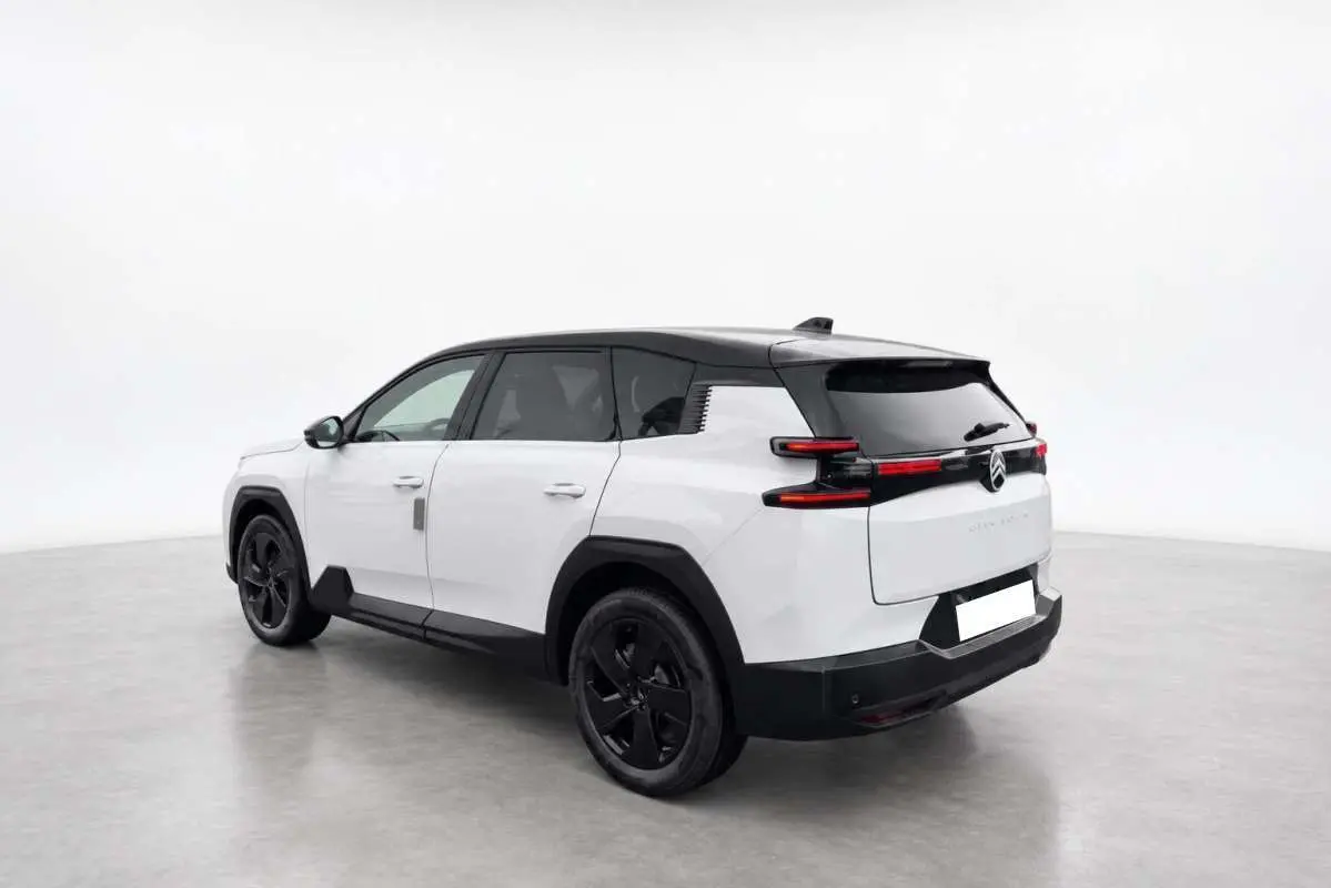 Vue 3/4 arrière droite du Citroën C5 Aircross Hybrid blanc avec toit noir et jantes noires dans un studio lumineux.
