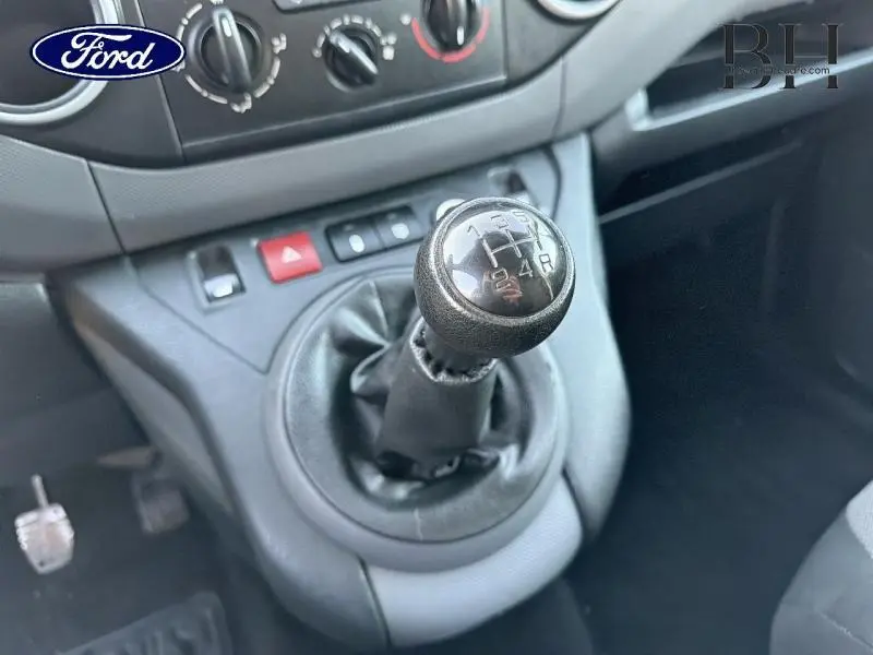 Gros plan sur le levier de vitesses manuel noir dans l'habitacle d'un Citroën Berlingo blanc, avec console centrale et commandes visibles.