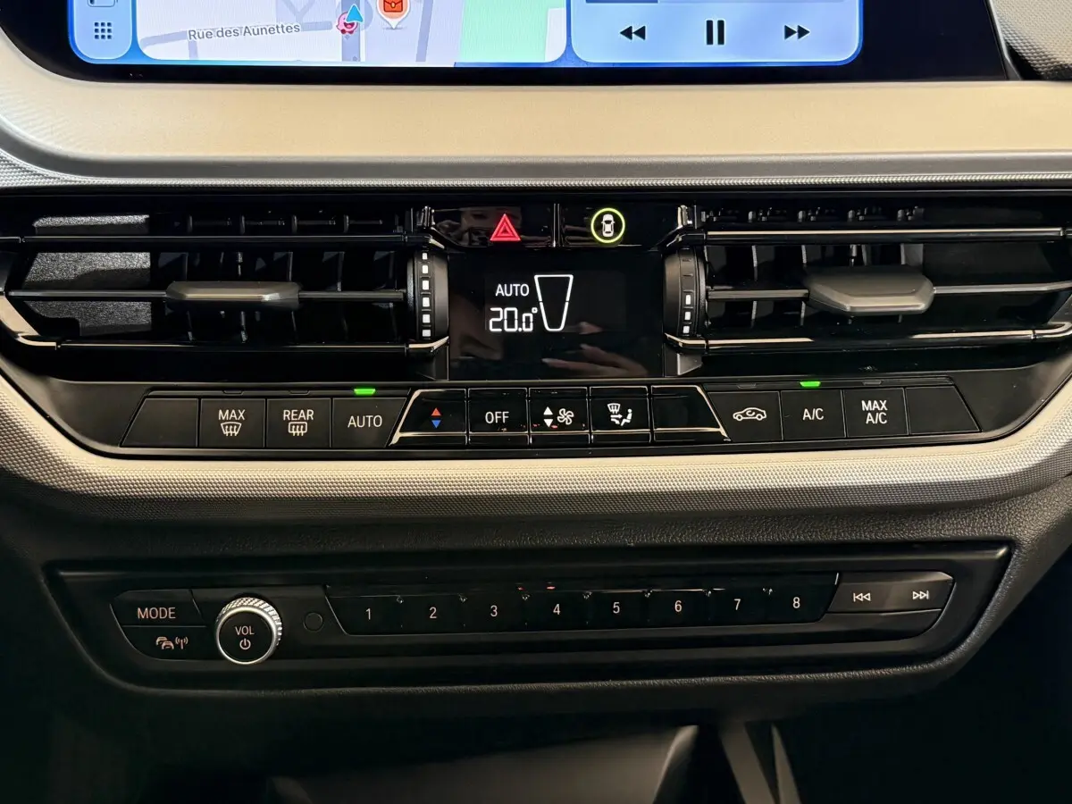 Gros plan sur la console centrale de la BMW Série 1 116i Business Design 2023, avec commandes climatisation et écran tactile visible.