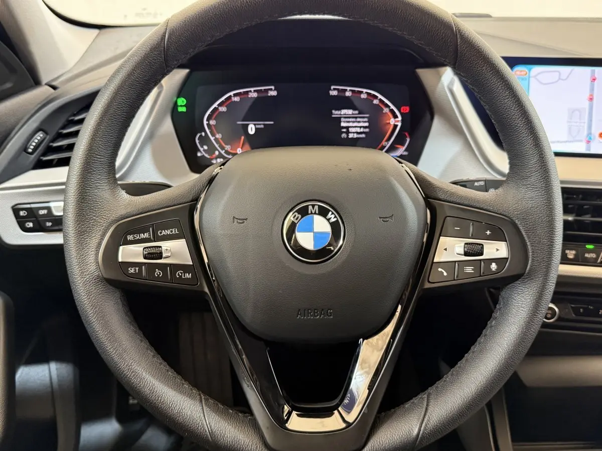 Vue rapprochée du volant cuir noir d’une BMW Série 1 116i 2023 avec tableau de bord digital et écran tactile latéral.