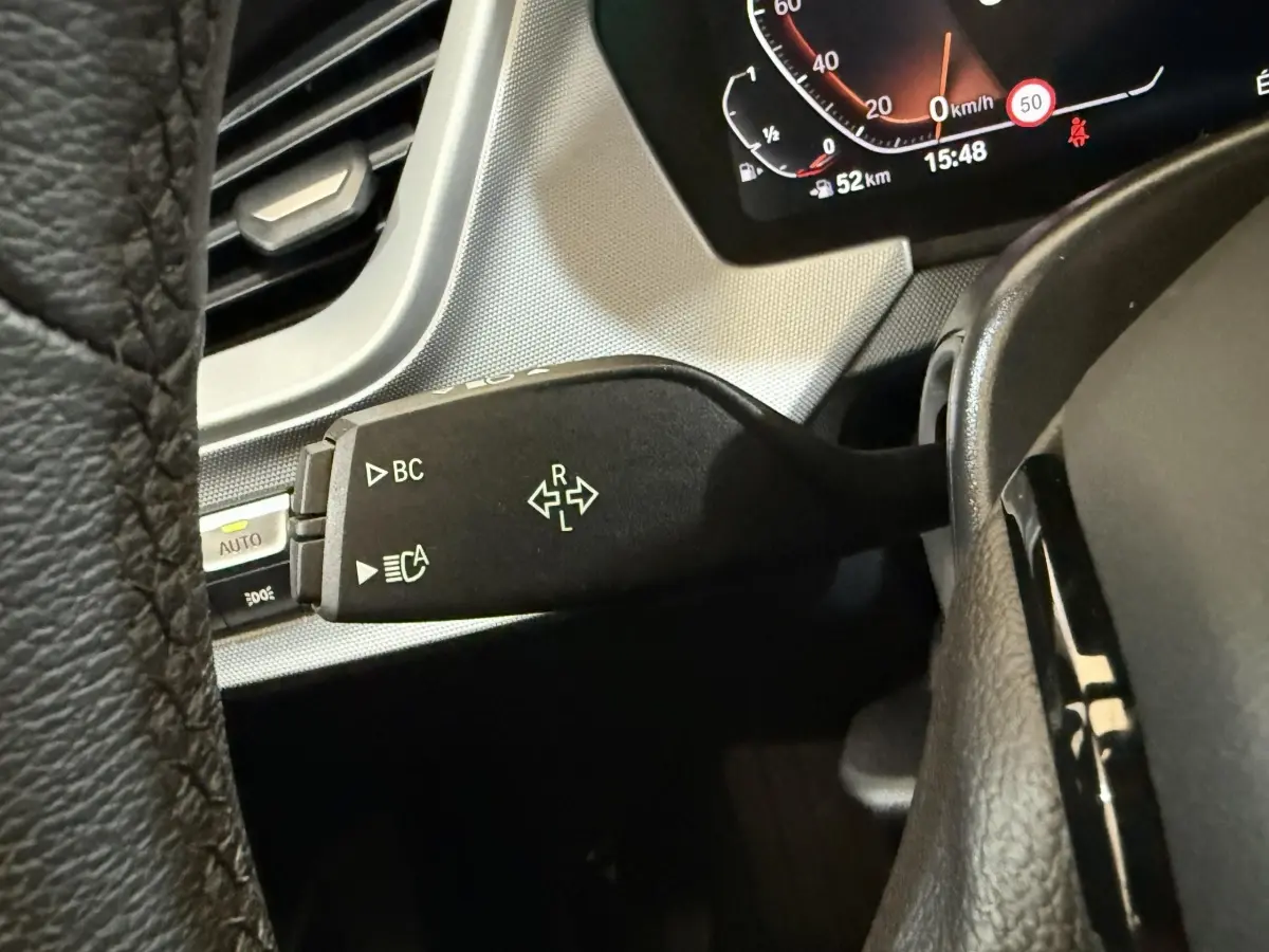 Gros plan sur la commande de clignotant et tableau de bord numérique d'une BMW Série 1 116i bleu, intérieur noir.