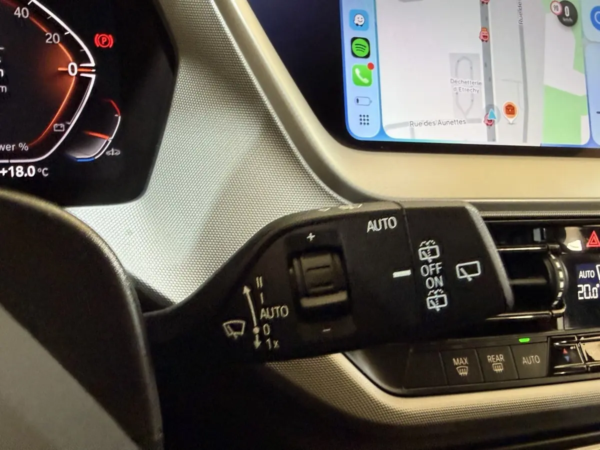 Gros plan sur la commande d’essuie-glace à gauche du volant dans l’habitacle d’une BMW Série 1 116i bleu, écran tactile visible.