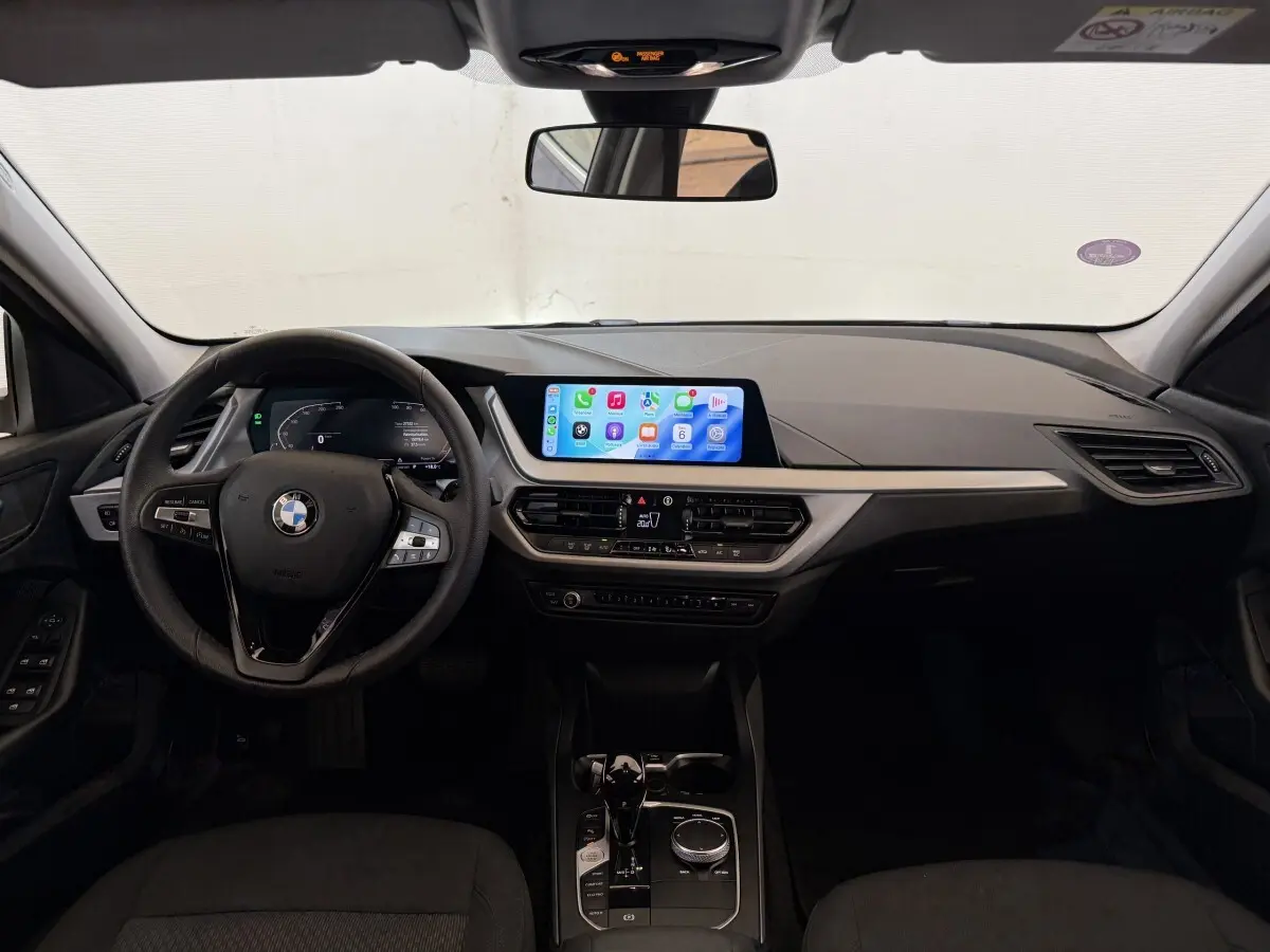 Vue intérieure frontale du tableau de bord noir de la BMW Série 1 116i 2023 avec écran tactile central et volant cuir multifonctions.