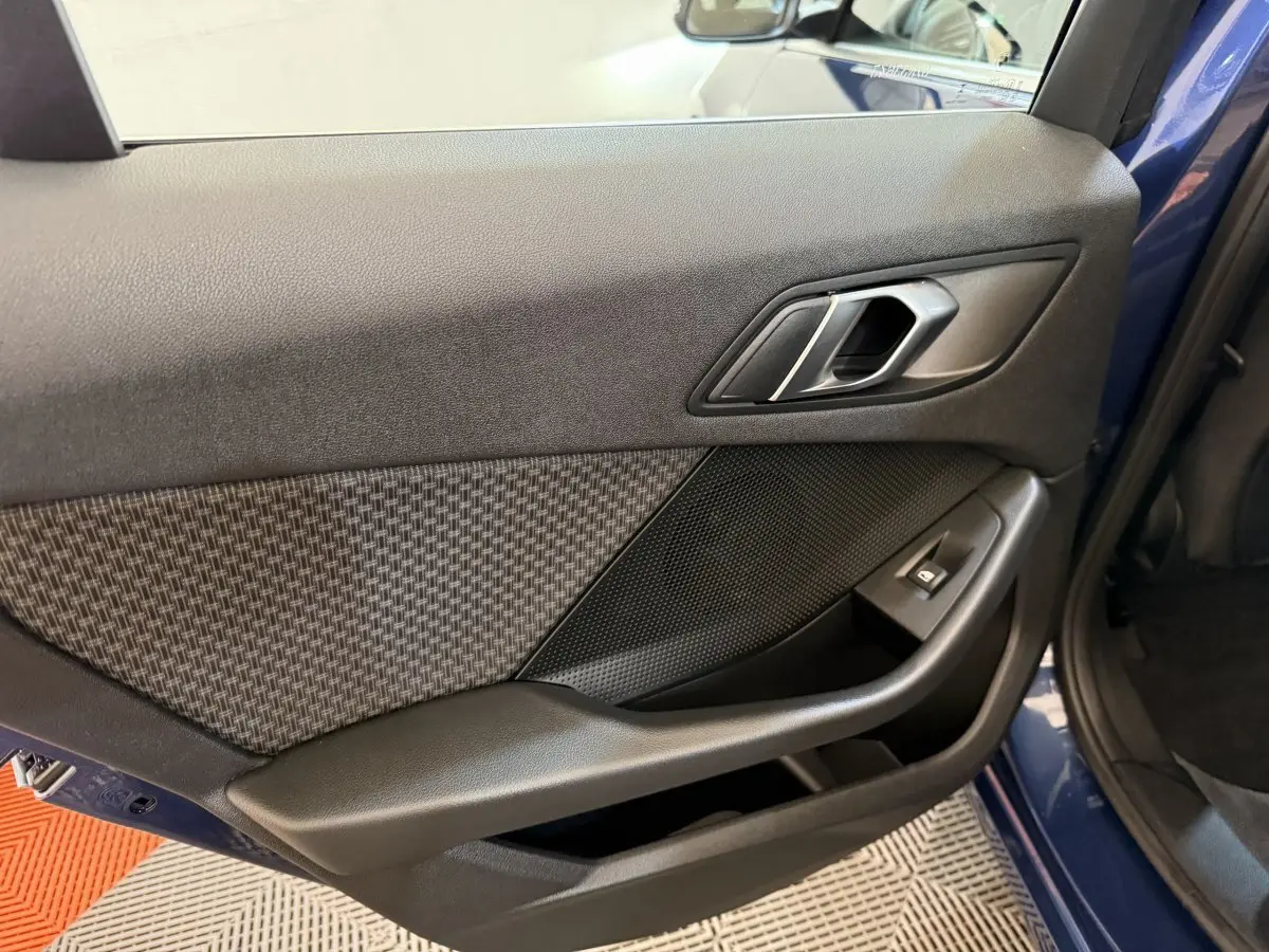 Gros plan sur la porte arrière droite bleu de la BMW Série 1 116i 2023 avec habillage tissu et commande de vitre noire.