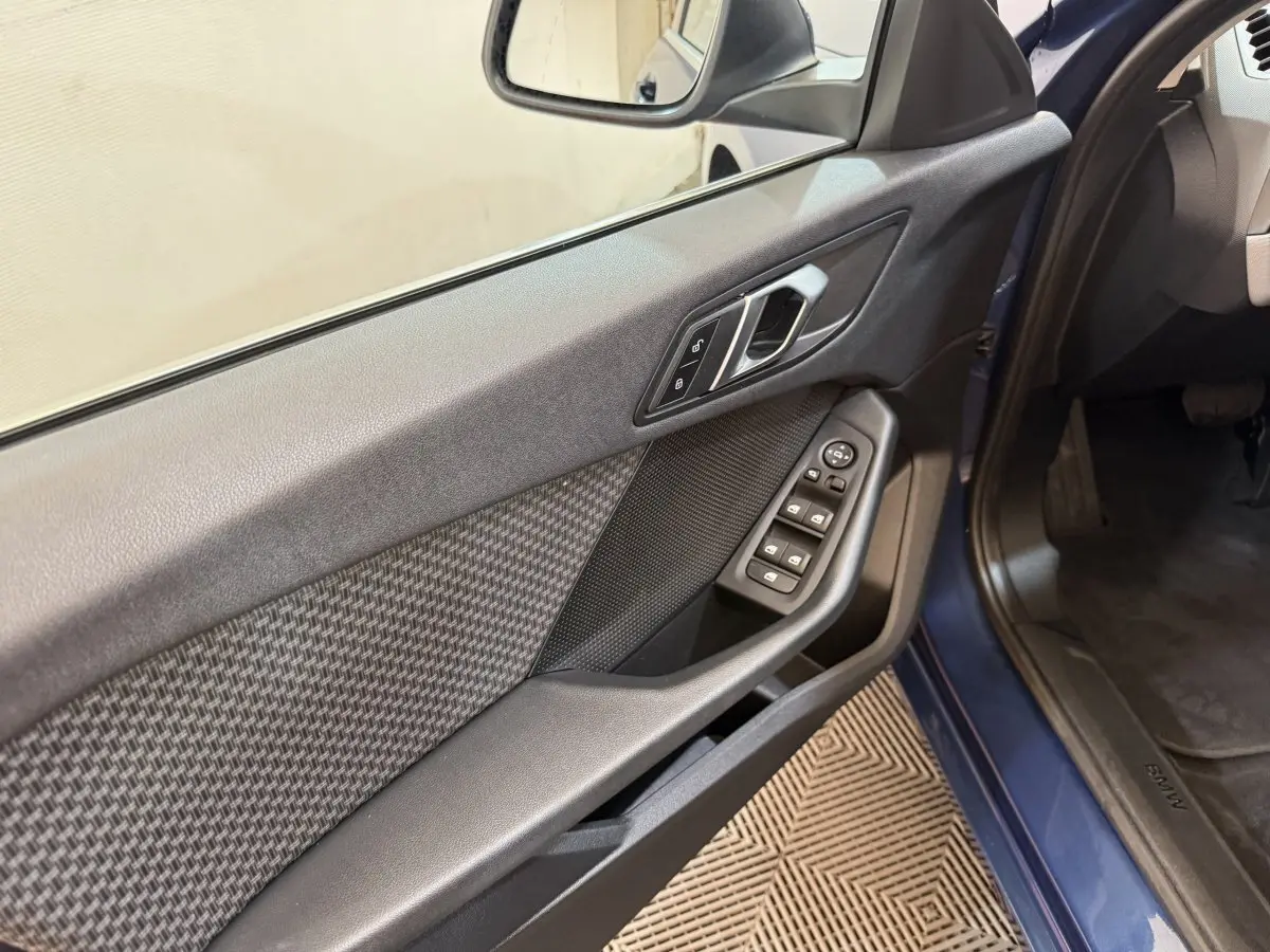 Vue intérieure côté gauche de la porte avant d’une BMW Série 1 bleu 2023 avec commandes de vitres et serrure.