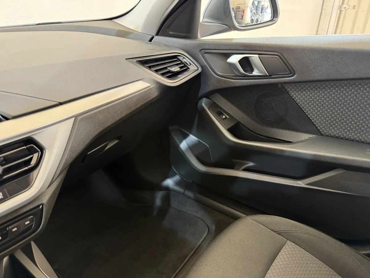 Vue intérieure côté passager de la BMW Série 1 116i Business Design 2023, avec tableau de bord et porte en tissu noir.