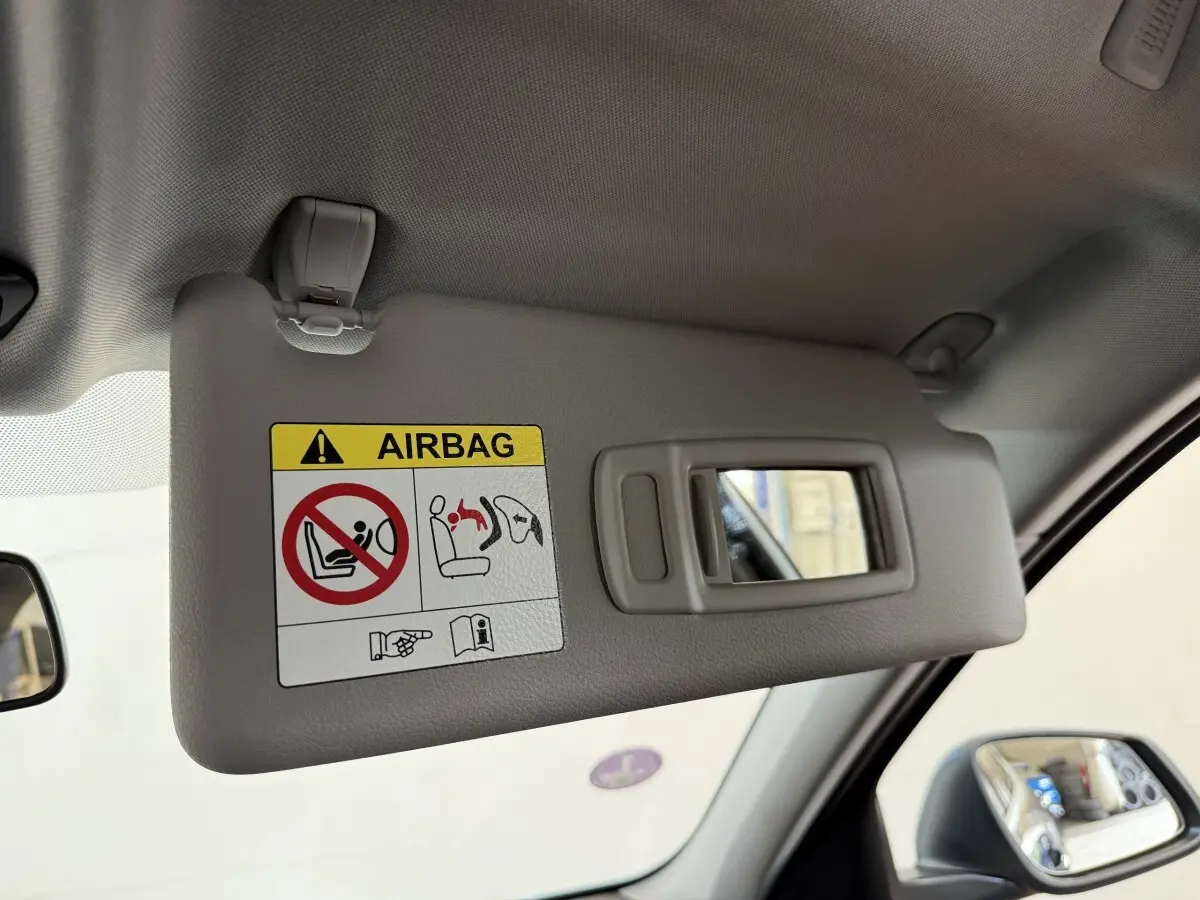 Vue intérieure côté conducteur sur le pare-soleil gris avec miroir et avertissement airbag dans une BMW Série 1 bleu 2023.