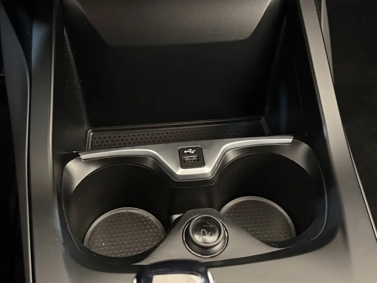 Gros plan sur les porte-gobelets noirs avec prise USB et allume-cigare dans la console centrale d'une BMW Série 1 116i.