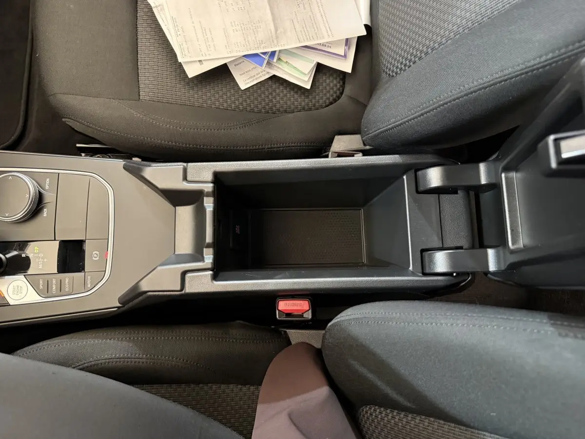 Vue plongeante sur la console centrale noire et les sièges tissu gris foncé de la BMW Série 1 116i 2023.