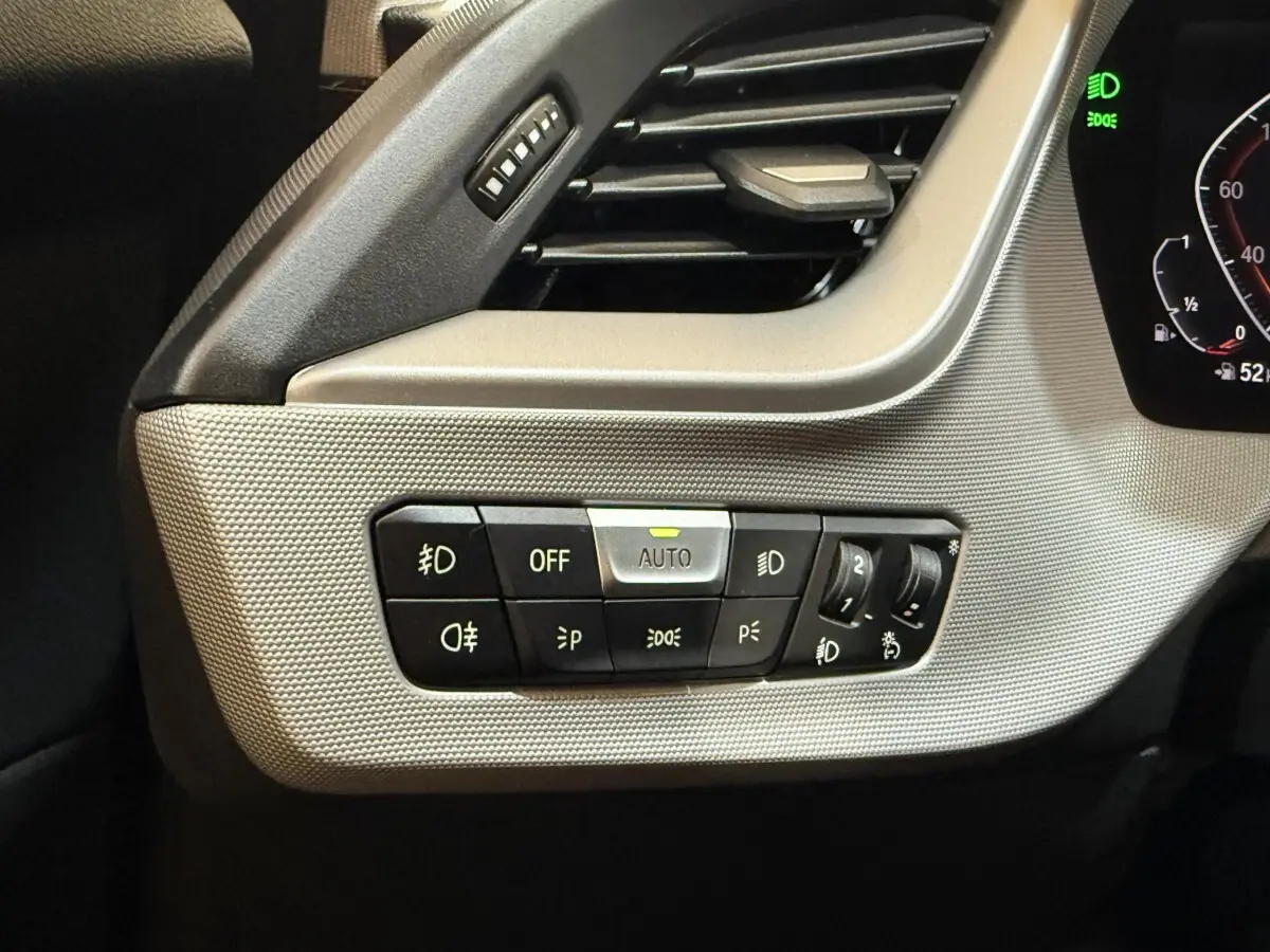 Gros plan sur les commandes d’éclairage à gauche du tableau de bord de la BMW Série 1 116i bleu 2023.