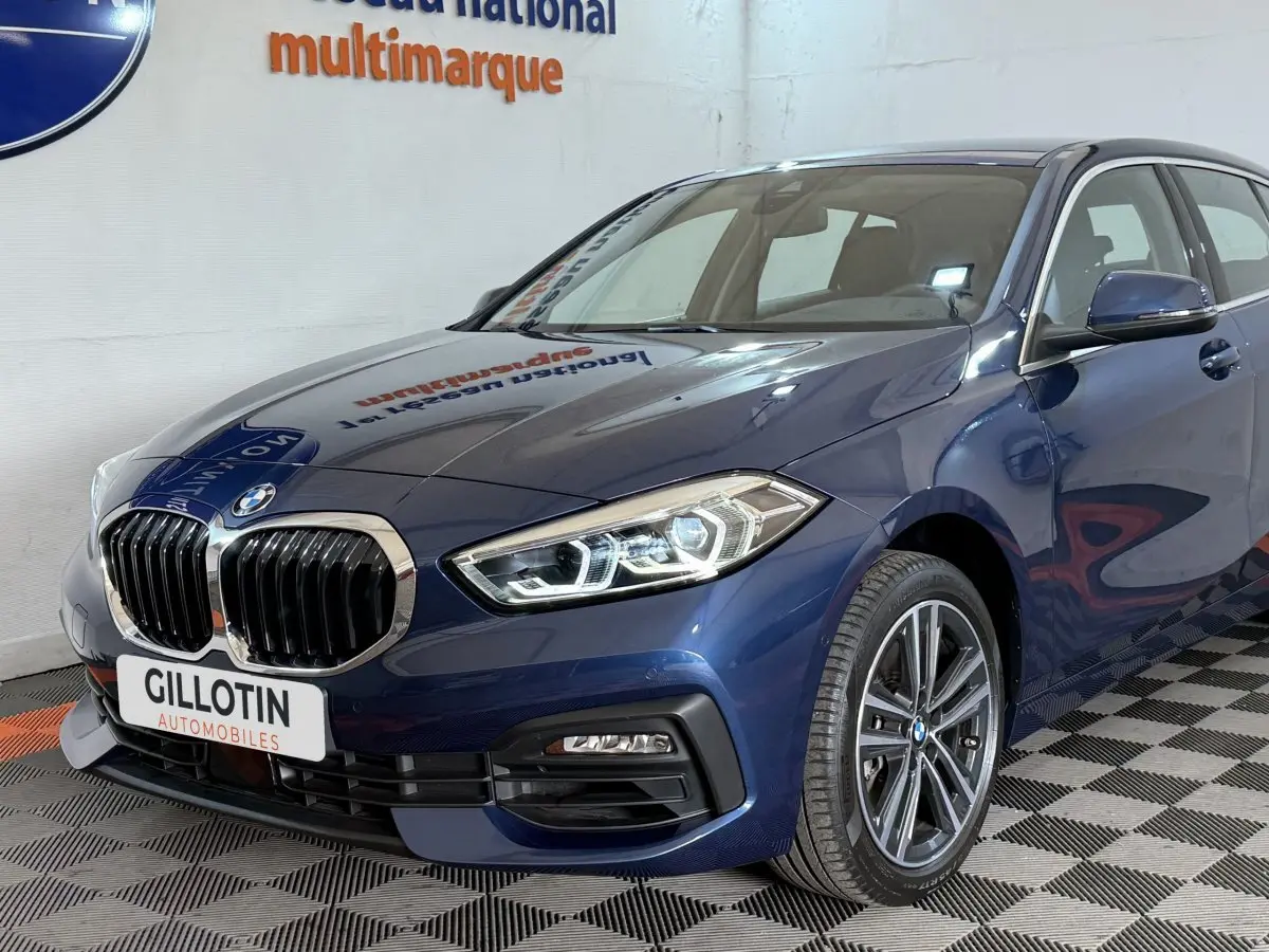 BMW Série 1 116i bleu vue 3/4 avant droit, mettant en valeur ses phares LED et calandre chromée.