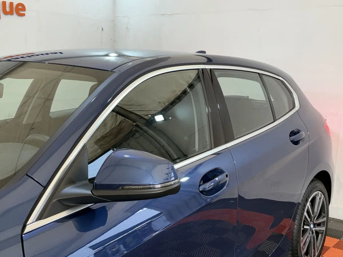 Vue côté gauche arrière d’une BMW Série 1 116i Business Design bleu avec rétroviseur et jantes visibles.