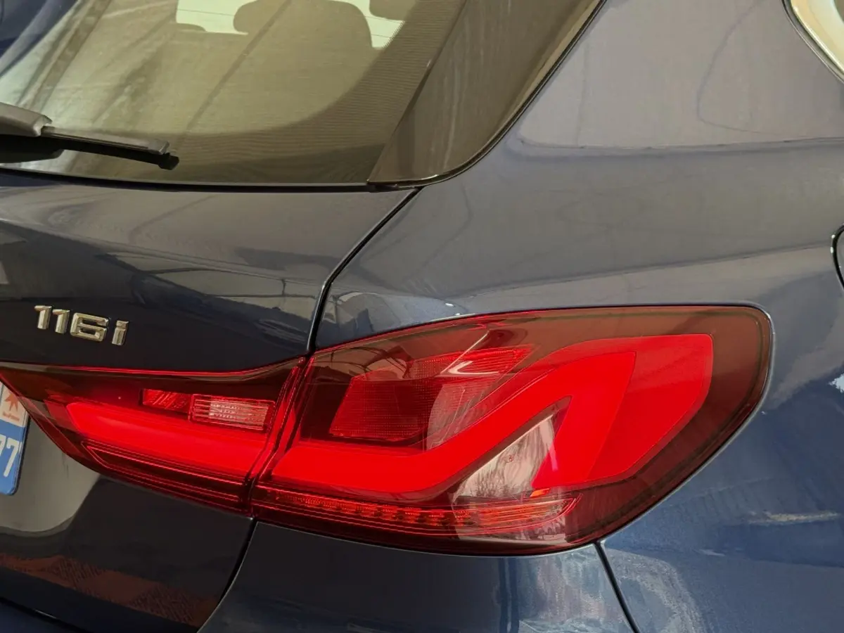 Gros plan sur le feu arrière droit rouge d'une BMW Série 1 116i bleu métallisé, avec logo 116i visible sur la malle.