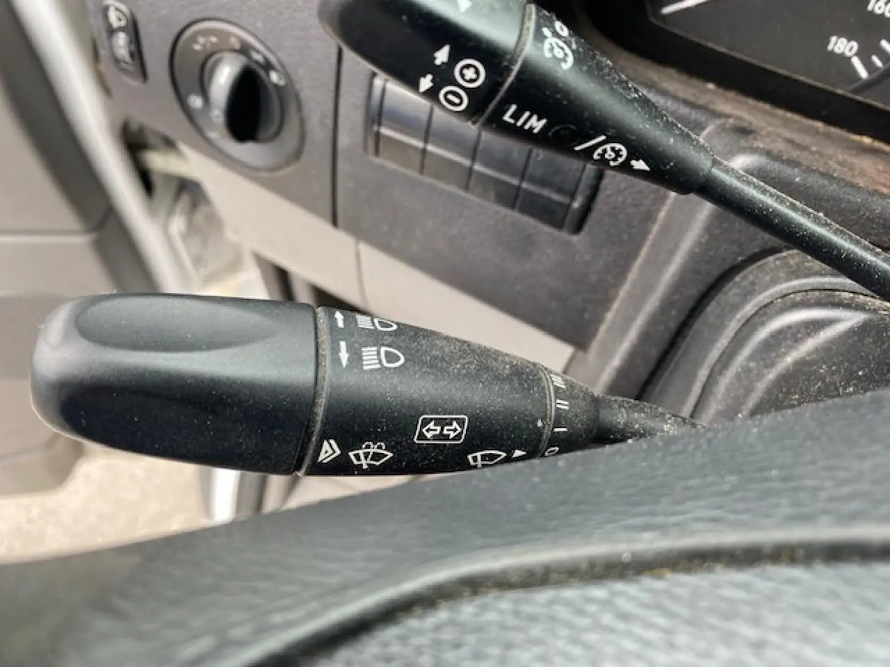 Gros plan sur les commandes de régulateur et limiteur de vitesse du Mercedes Sprinter Fourgon blanc, intérieur côté conducteur.