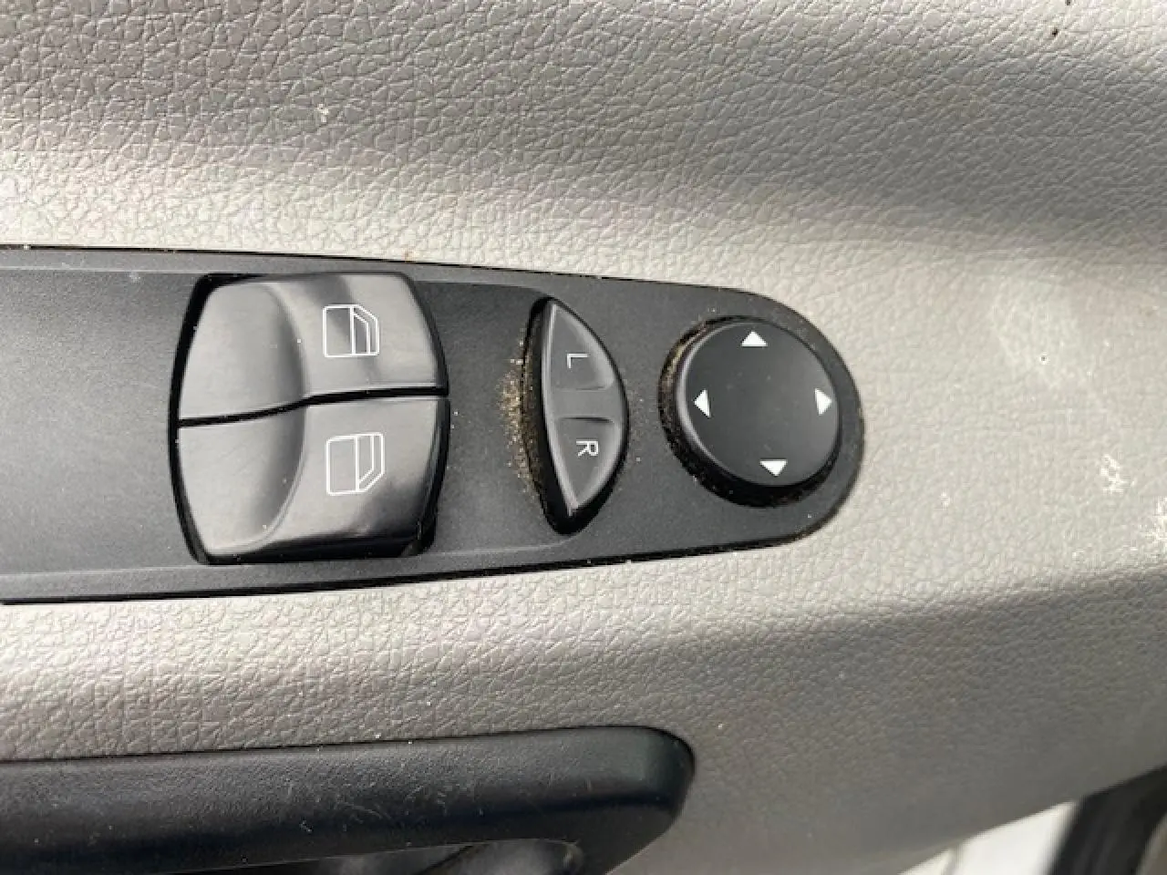 Gros plan sur les commandes électriques des vitres et des rétroviseurs du Mercedes Sprinter blanc, côté conducteur.