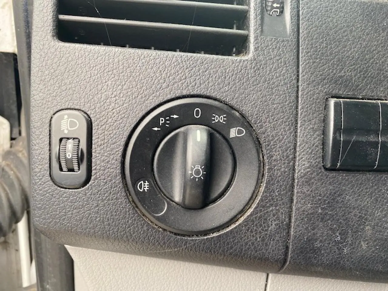 Gros plan sur le bouton de commande des phares du Mercedes Sprinter Fourgon blanc, tableau de bord noir texturé.