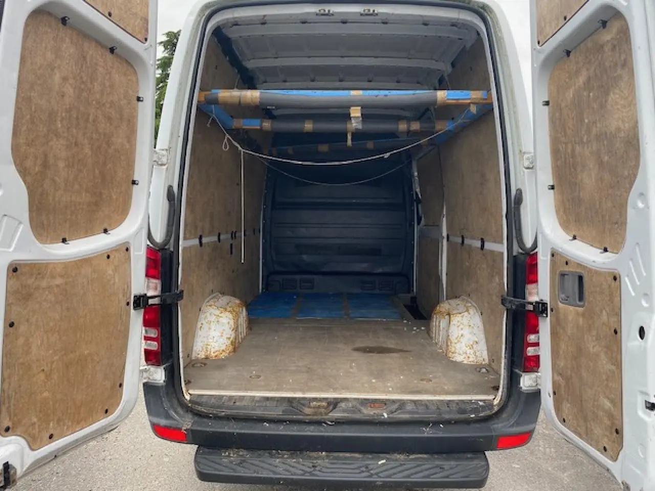 Vue arrière ouverte du Mercedes Sprinter blanc 2015, montrant l'intérieur utilitaire avec aménagements en bois et structure métallique.