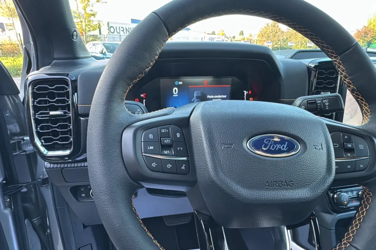 Vue rapprochée du volant cuir noir avec surpiqûres marron du Ford Ranger PHEV 281 Wildtrak, tableau de bord numérique visible.