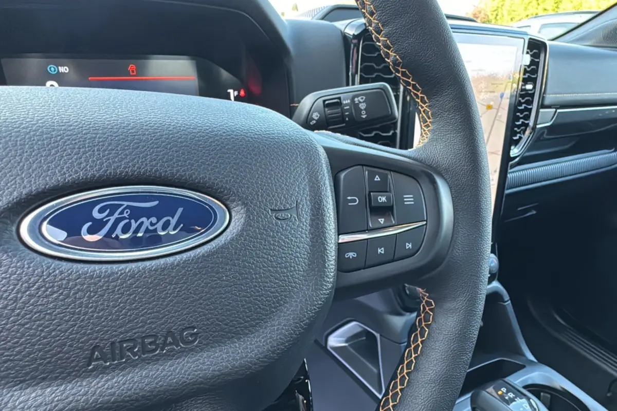 Gros plan sur le volant en cuir noir avec surpiqûres orange du Ford Ranger PHEV 2025, tableau de bord et écran tactile visibles.