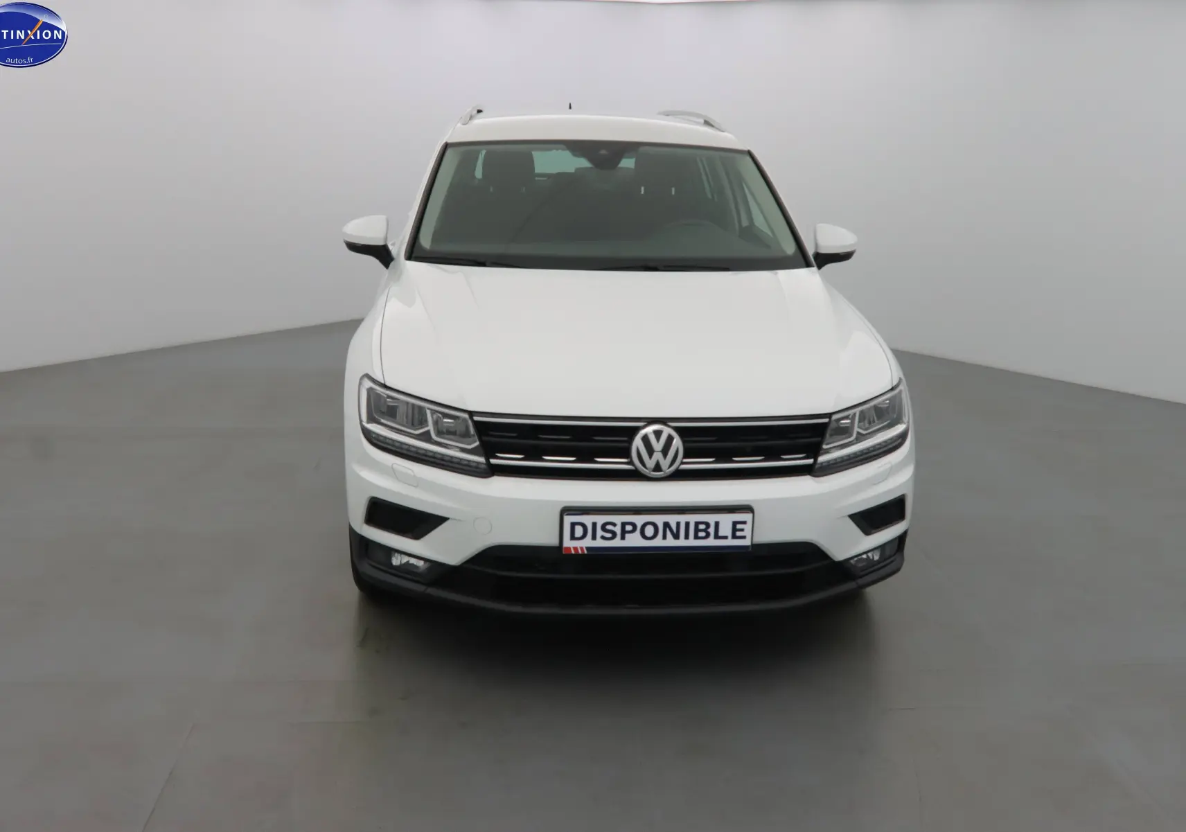 Vue frontale d'un Volkswagen Tiguan blanc 2019 avec calandre noire et feux LED allumés.