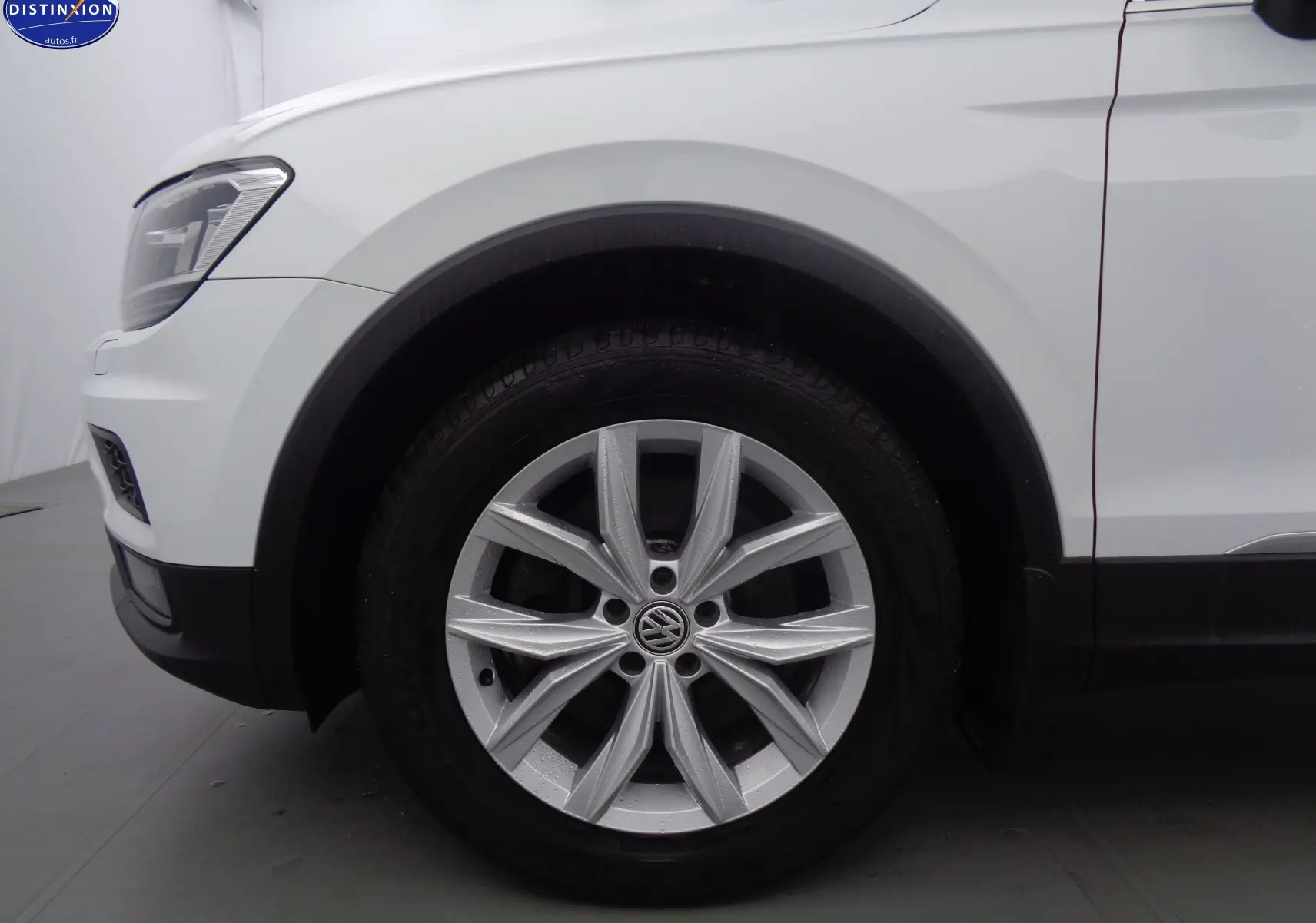 Gros plan sur la roue avant gauche d'un Volkswagen Tiguan blanc 2019, mettant en valeur la jante alliage et le passage de roue.