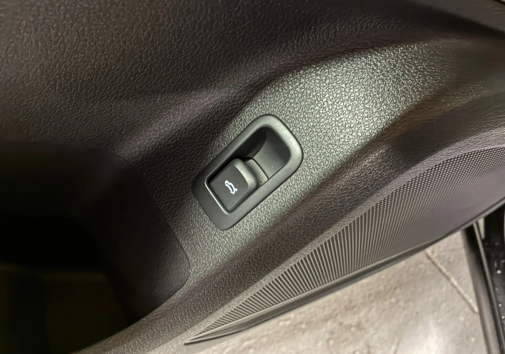 Bouton d'ouverture du coffre intégré dans la garniture intérieure noire de la porte d'un Audi Q2 35 TFSI 2023.